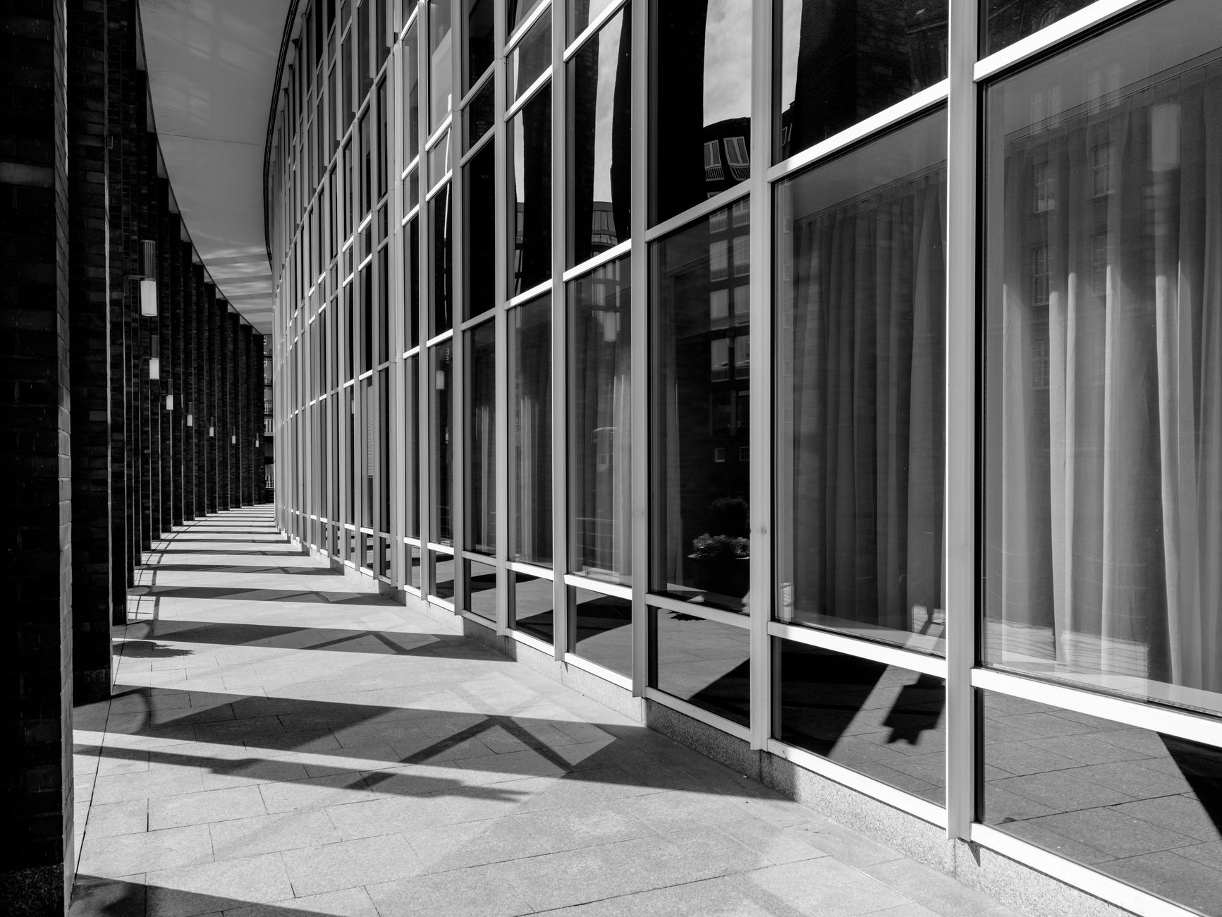 A glass office facade running down a covered walkway in hard late daylight